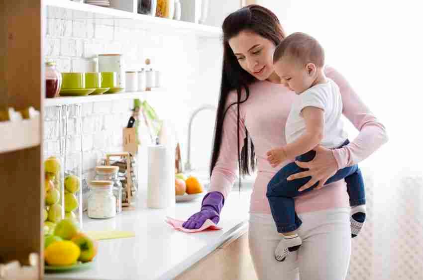 Domestic chores at maternity leave. Young mother with baby boy cleaning kitchen at home, free space